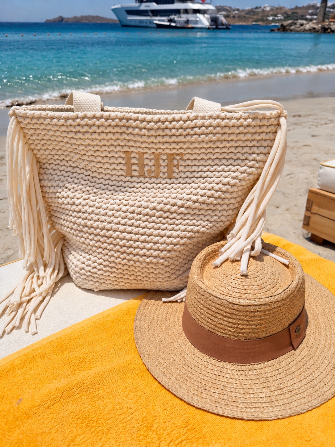 Monogrammed woven tote beside a straw hat at the beach