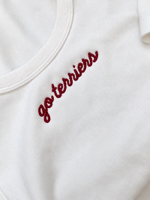 Close detail of burgundy go terriers script embroidered on a white sleeveless top.