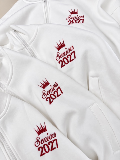 Four overlapping white quarter-zip tops with burgundy crowns and Seniors 2027 embroidery.
