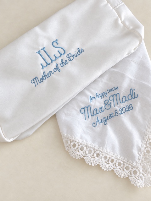 White satin Mother of the Bride pouch beside a lace handkerchief embroidered for happy tears, Max and Madi, August 8 2026.