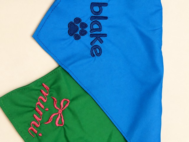 Blue bandana embroidered blake with a navy paw print, overlapping a green bandana embroidered mimi with a pink bow.