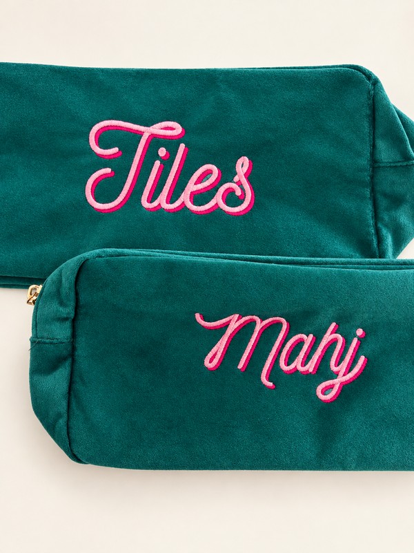 Two teal velvet pouches embroidered Tiles and Mahj in pale pink script with deeper pink stitched shadows.